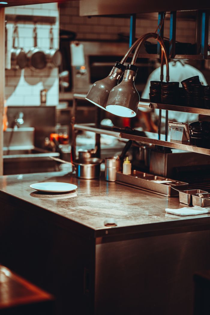 Services A modern Tokyo restaurant kitchen with stainless steel surfaces and hanging lamps.