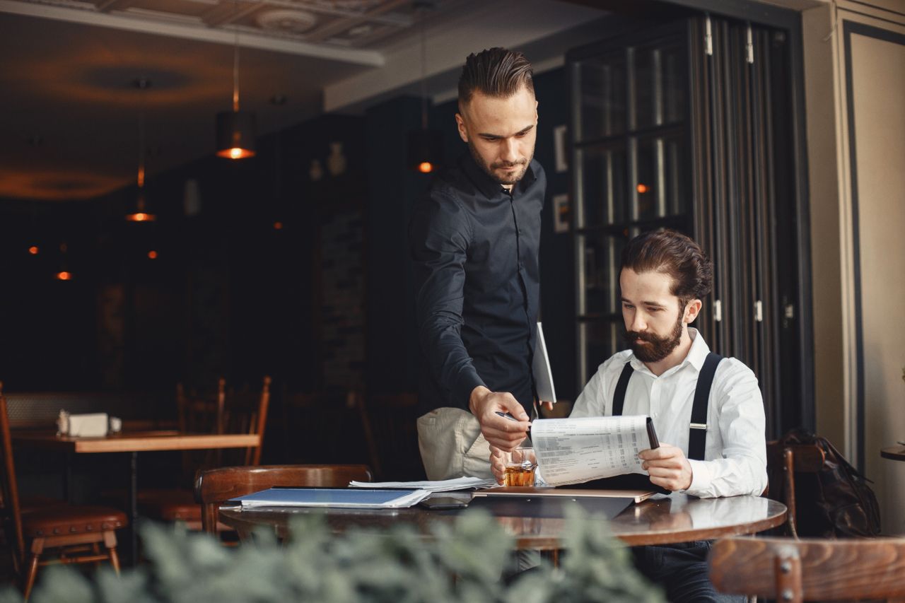 Mastering the First Impression: Your intriguing post title goes here Two men discuss business over documents in a cozy, stylish restaurant.